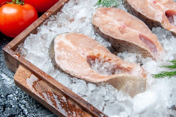 bottom-view-raw-fish-slices-with-ice-wood-board-fresh-tomatoes-table